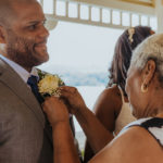 closeup of grandmother of bride pinning the boutonniere to the groom's jacket.