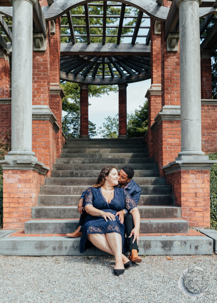 shot of brides sharing a kiss, sitting on steps if italian gardens at vanderbilt mansion.