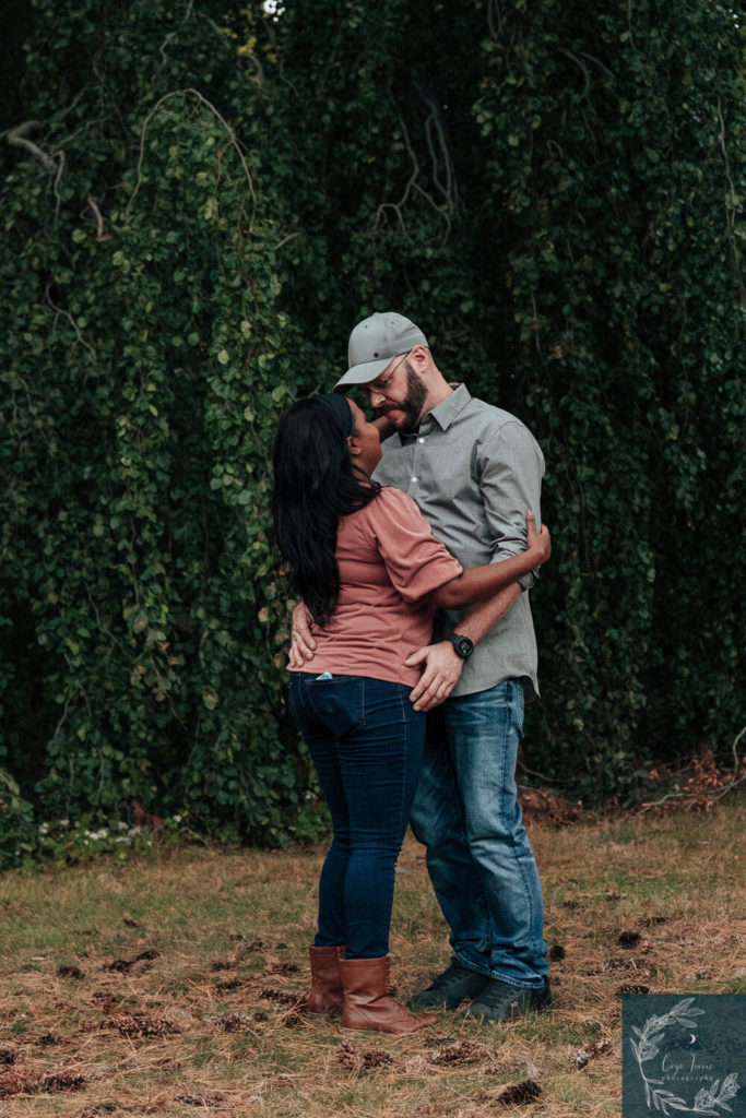 Newly engaged couple embraces in front of large tree. Engagement Session at Vanderbilt Mansion