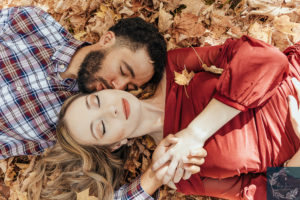 newly engaged couple enjoys laying together in the fall foliage, holding hands.