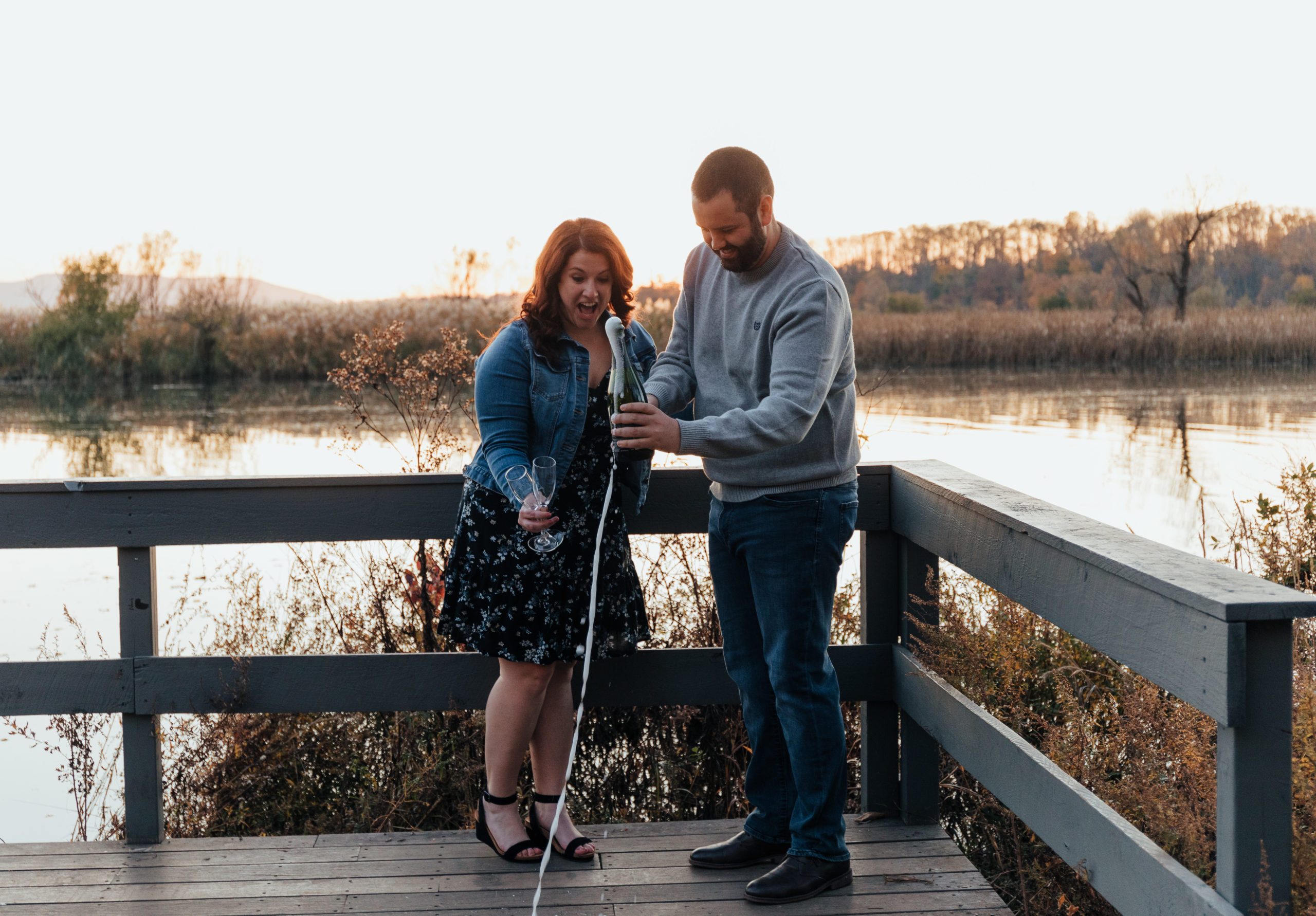 Newly engaged couple celebrates their engagement by popping a bottle of champagne.