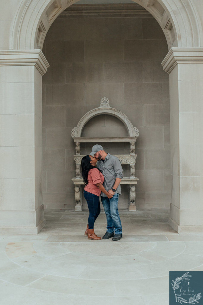 couple sharing a kiss under a stone archway. Engagement Session at Vanderbilt Mansion