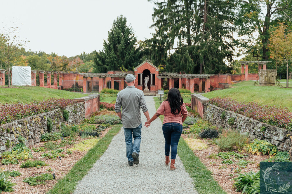 couple holding hands and walking away from the camera down a path in a garden.