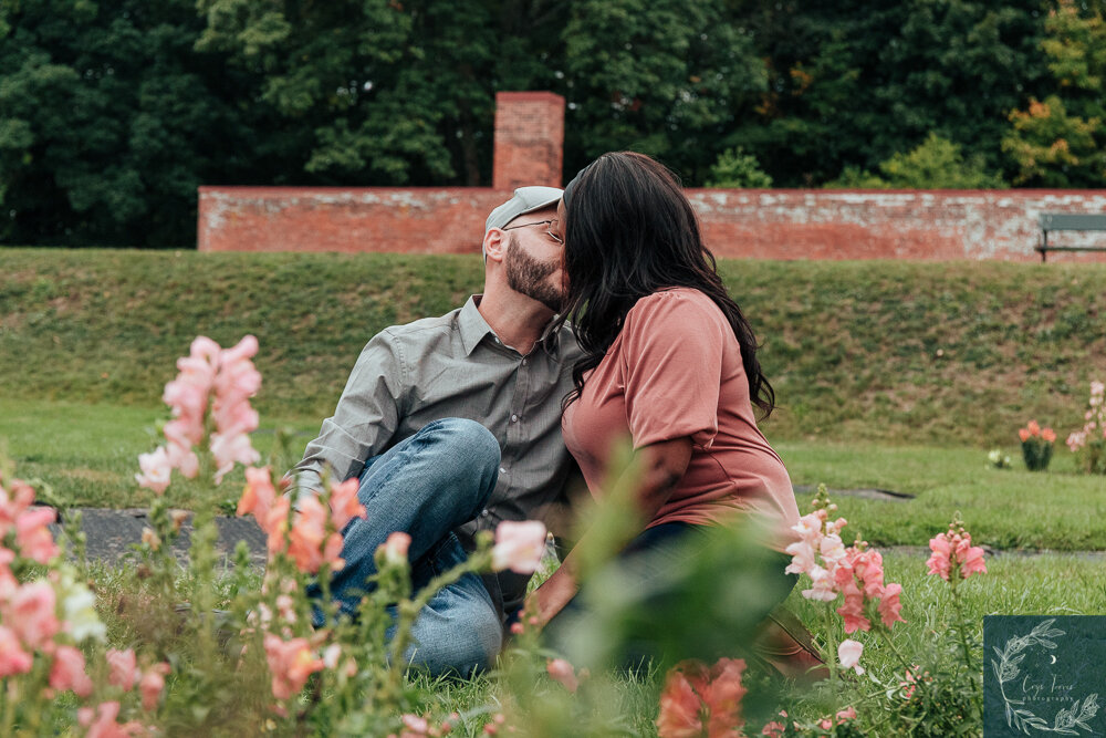 couple sitting in grass sharing a romantic kiss. Engagement Session at Vanderbilt Mansion