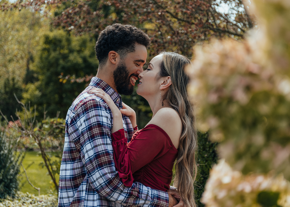 couple smiling holding each other close surrounded by flowers at orange county arboretum