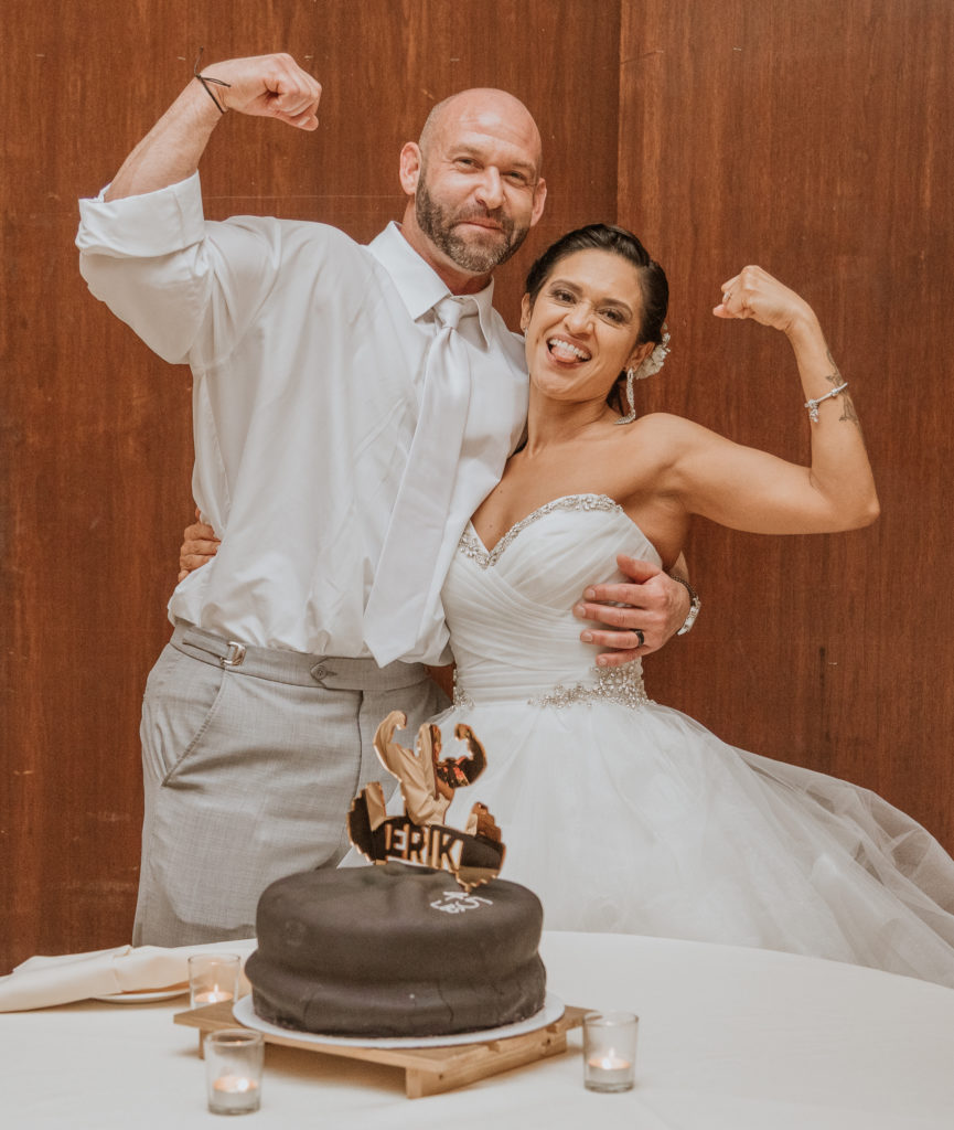 fitness couple posing in front of groom wedding cake thayer hotel